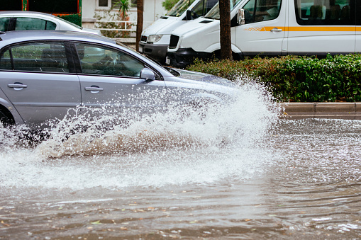 Splash by a car as it goes through flood water, Cars on a flooded city road at the rain day.