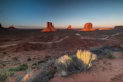 Sunset over the three classic buttes with roads and some vegetation in Oljato-Monument Valley, AZ, United States