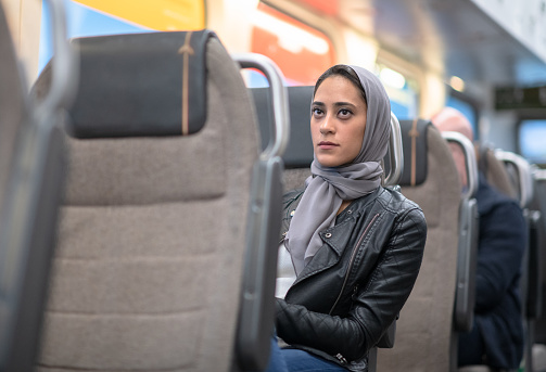 A beautiful Muslim woman wearing a hijab is sitting at her seat in the bus/train and is waiting for the other passengers to come on board.