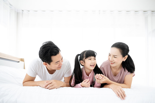 Happy asian family people leisure in bedroom together. Father and mother with daughter relaxing on bed and enjoy funny