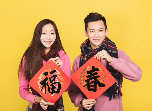 happy asian couple showing red couplets and celebrating chinese new year . chinese text: spring  luck