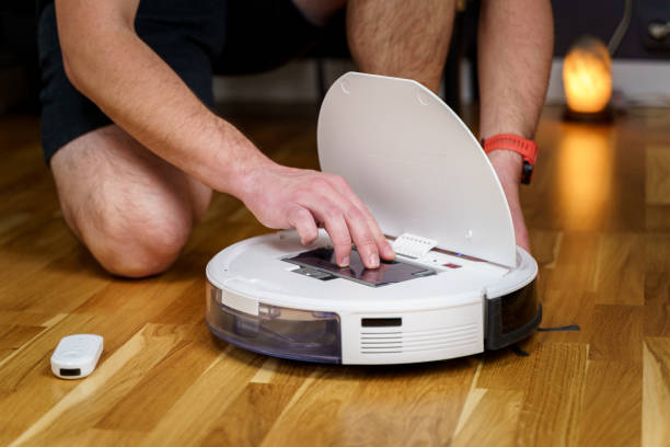 istock Caucasian young man doing white robot vacuum cleaner maintenance. Autonomous wireless modern vacuum cleaner. Male repairing robot cleaner home on floor. Vacuum cleaner robot repair concept 1295892934