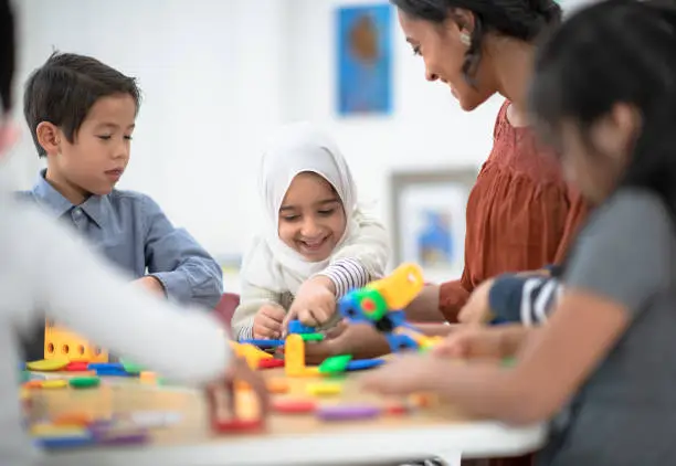 A multi ethnic group of preschool children are working together to build using colourful plastic toys.