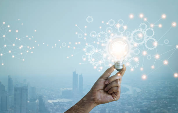 istock Double exposure. New ideas. Innovation and creativity. Technology and development. Businessman hand holding light bulb and cog wheel on city background. Blue tone. 1295897670