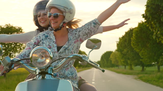 SLOW MOTION Female friends enjoy riding retro moped