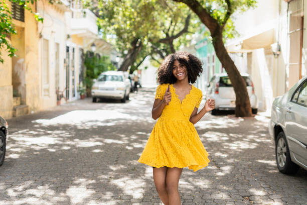 jeune femme noire avec le cheveu bouclé, dans la robe jaune et avec des modèles, attitude, rire, heureux - women dress black young women photos et images de collection