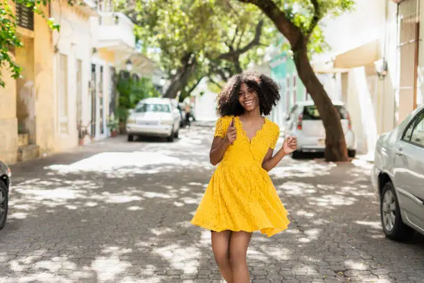 Photo of Young black woman with curly hair, in yellow dress and with styles, attitude, laughing, happy