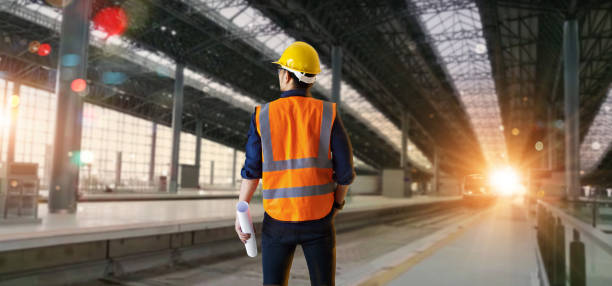 Back view of industrial engineer manager standing and holding a blueprints and checking structure and of construction railway site of high speed background. Technology and engineering. transportation and logistics.