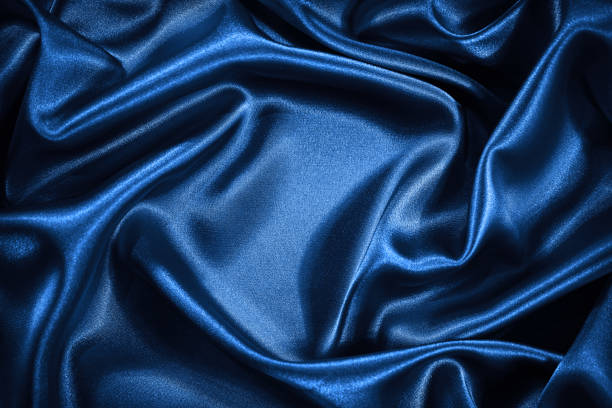 istock Black silk satin background. Shiny fabric with wavy folds. 1295910832