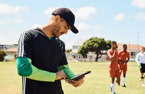 Shot of a soccer coach using a digital tablet while out on the field