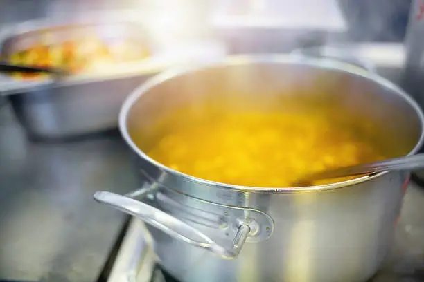 Preparation of the first course in the dining room. Soup or chowder is cooked in an aluminum pot on an electric stove. Food background close up