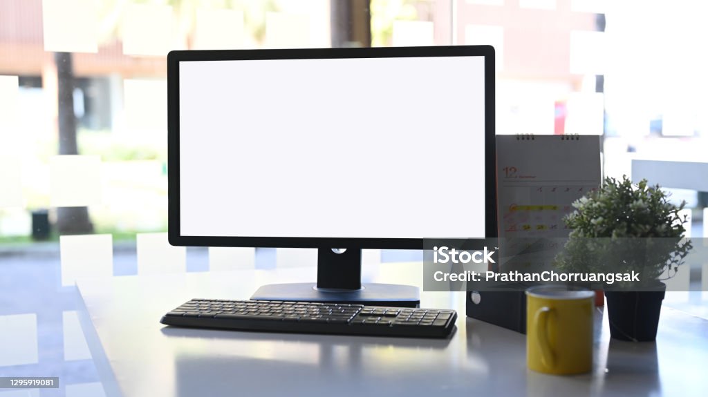 Front view computer with white screen, coffeecup, plant and calendar on white table. Computer Monitor Stock Photo