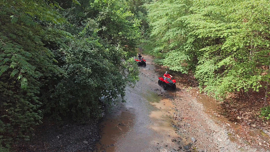 Driving off-road vehicles thru a small water stream drone point of view