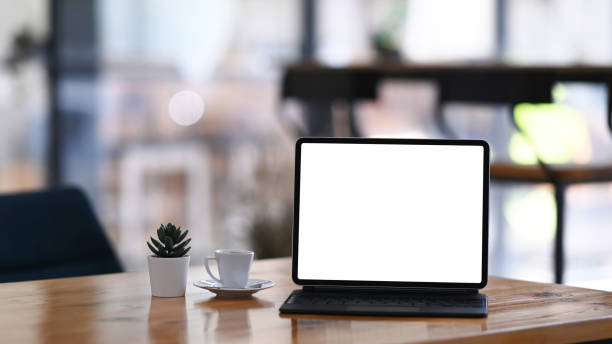 istock Mock up tablet computer, cup of coffee and cactus on wooden table. Blank screen for graphic display montage. 1295920359