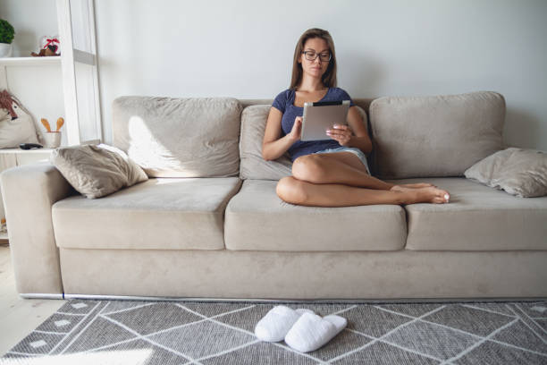 istock Young woman sitting on sofa and using tablet at home 1295922319