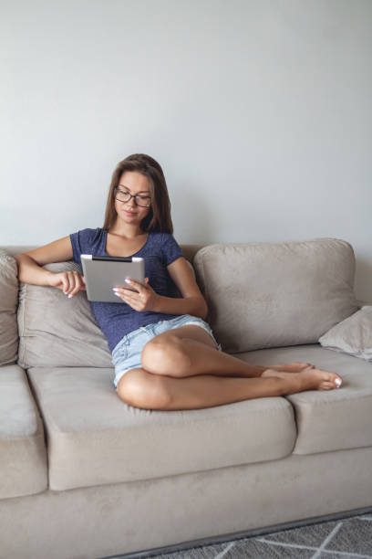istock Young woman sitting on sofa and using tablet at home 1295922327