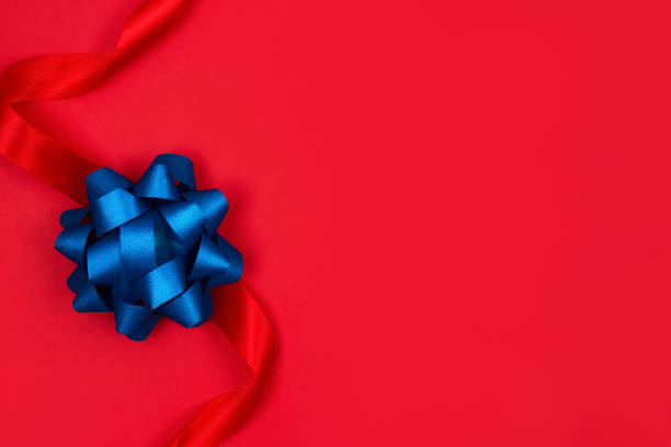 istock Top view on decorative blue ribbon bow on red background with copy space for text. Giving presents concept. Greeting card or holidays sale background. Selective focus 1295923133
