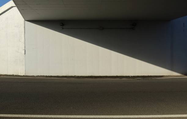 istock White concrete wall under an underpass divided in two obliquely by a shadow. Asphalt road in front. 1295924575