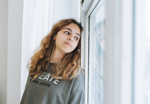 Beautiful sad unhappy teenager girl with curly hair sitting on the window sill Beautiful sad unhappy teenager girl with curly hair sitting on window sill sad 15 years old girl stock pictures, royalty-free photos & images
