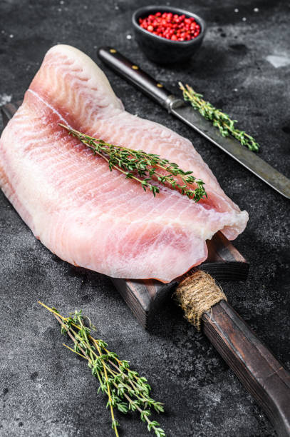 istock Fresh raw white fish fillet Pangasius with spices. Black background. Top view 1295926322