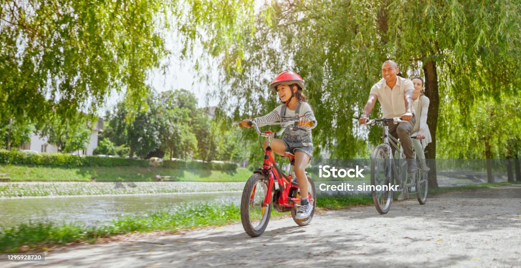 Family riding bicycle Smiling family riding bicycle together on footpath by lake in public park. Cycling Stock Photo
