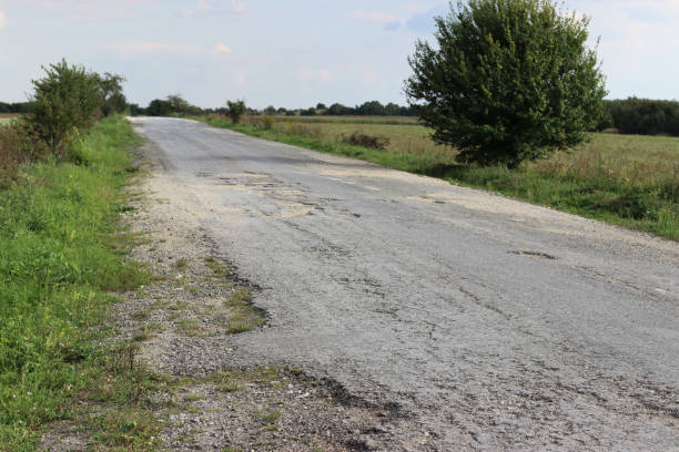 istock Abandoned field road covered with destroyed asphalt pavement 1295932242