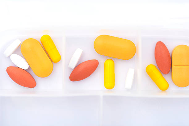 istock Opened pill box with yellow, red pills on white table 1295932945
