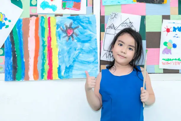 Cheerful young girl painting on the wall,Art lesson in kindergarten,Portrait of adorable little girl smiling happily while enjoying art and craft lesson in pre school working together