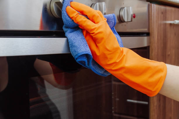 Hand with a microfiber cloth is being wiped on the outside of the electric oven. An orange-gloved hand with a microfiber cleaning cloth is being wiped on the outside of the electric oven. The cleaning of the kitchen concept camping stove photos stock pictures, royalty-free photos & images