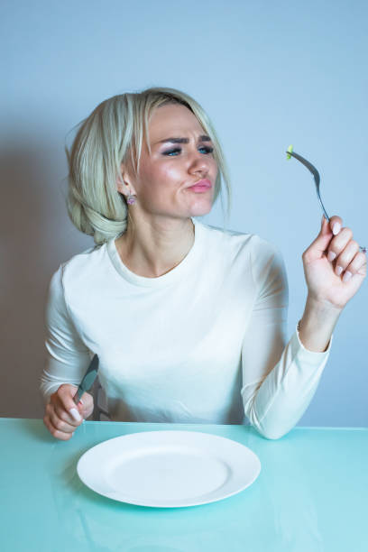 istock Sick girl sits at the table and eats a vegetable. 1295936549