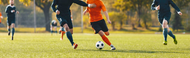 Horizontal image of football players running in a duel on a tournament match. Soccer forward player compete with defender. Anonymous football players kicking league game Horizontal image of football players running in a duel on a tournament match. Soccer forward player compete with defender. Anonymous football players kicking league game club football stock pictures, royalty-free photos & images