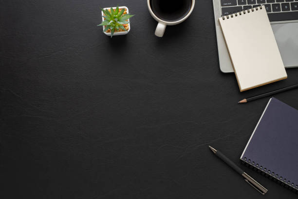 istock Top view above of Black leather office desk table with keyboard, notebook and coffee cup with equipment other office supplies. Business and finance concept. Workplace, Flat lay with blank copy space. 1295938046