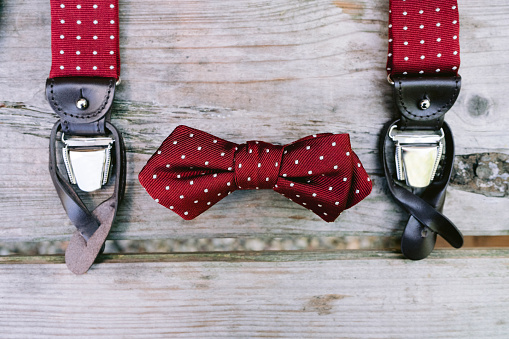 Braces and bow tie in red with white dots lie on a wooden table close-up