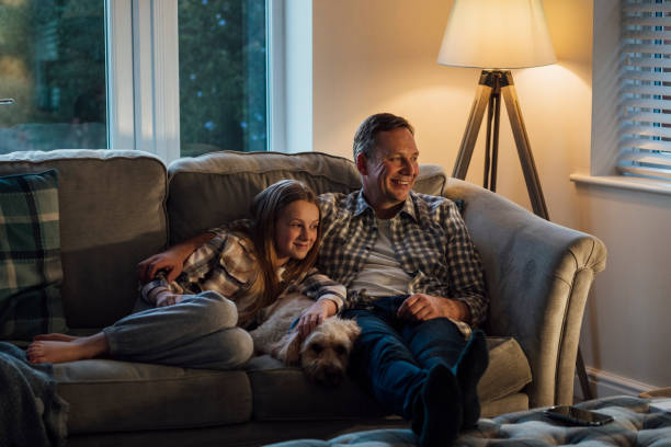 Movie Night with Dad A mid-adult caucasian father lying down on the sofa with his young daughter, they are watching a movie on the tv. cozy stock pictures, royalty-free photos & images