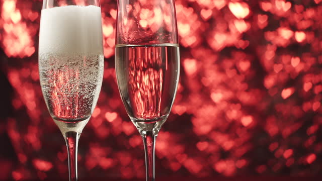 Champagne is poured into a glass on a red background with many hearts, close up.