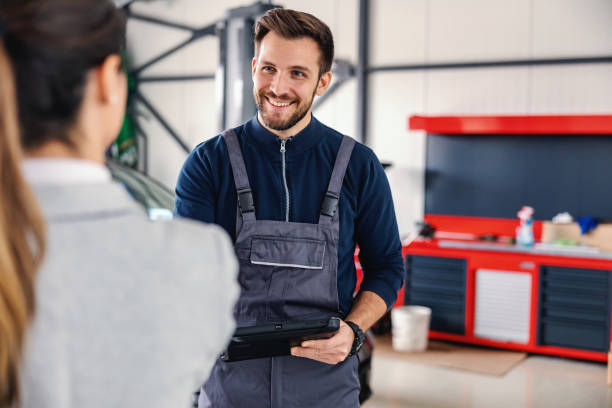 sorridente venditore di auto amichevole che parla con un meccanico e mostra il gesto della mano ok mentre si trova nel salone dell'auto. - independence business women manual worker foto e immagini stock