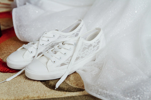 Bride's white sneakers are next her wedding dress. Charges of the bride