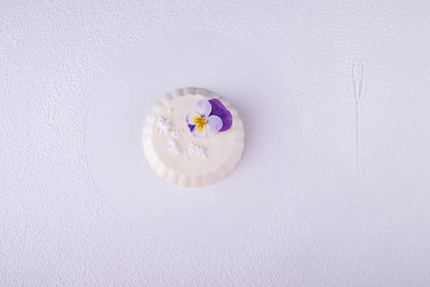 panna cotta of white cocolate and wipped cream decorated with edible violet flower over on white background with dessert spoon trace - wipped cream imagens e fotografias de stock