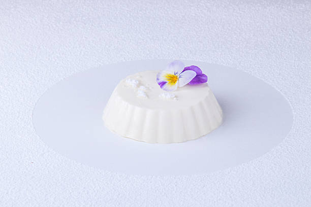 panna cotta of white cocolate and wipped cream decorated with edible violet flower over on white background with dessert spoon trace - wipped cream imagens e fotografias de stock
