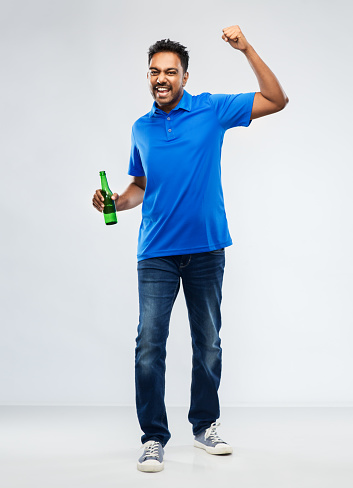emotion, expression and success concept - happy indian man or sports fan beer bottle celebrating victory over grey background