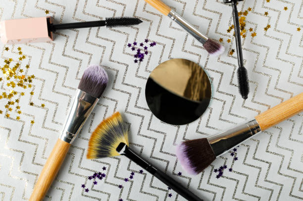Top view of round mirror, brushes for makeup and glitter on the grey surface