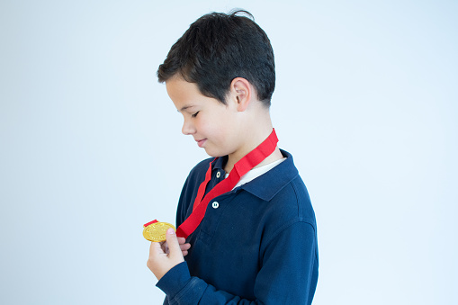 Young boy looking at his golden medal over white background.