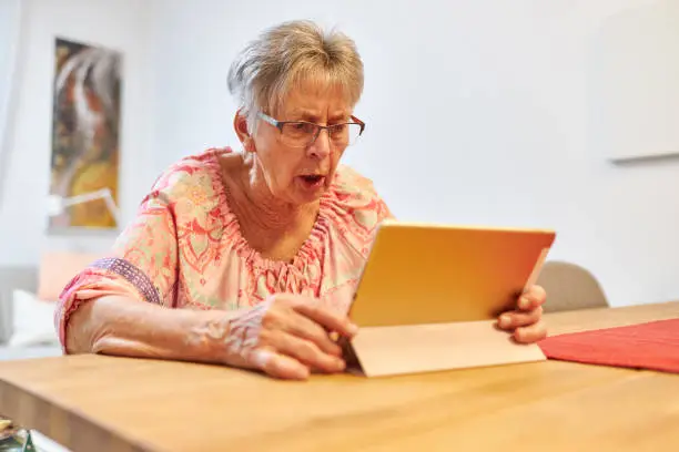 An 80-year-old senior works on her tablet and uses video telephony in her living room, high-resolution with copy space