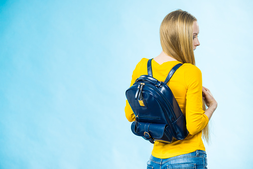 Blonde teenage girl going to school or college wearing stylish backpack. Outfit trendy accessories. On blue