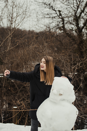 A young woman taking a selfie with a snowman in mountain