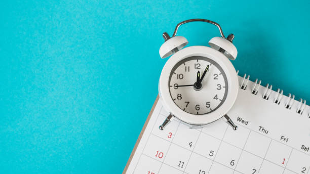 istock white analog alarm clock on blurred calendar with grunge blue background with copy space, business meeting schedule, travel planning or project milestone and reminder   concept ,panorama 1295959931