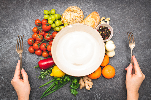 Fresh greens, vegetables and ingredients with plate in center and hands with silverware