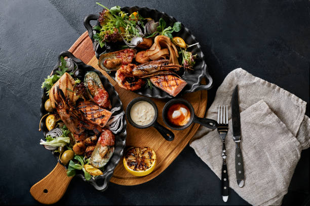 istock grilled seafood platter. Assorted delicious grilled seafood with vegetables. Grilled mixed bastards with pepper sauce and vegetables. Black background 1295961662