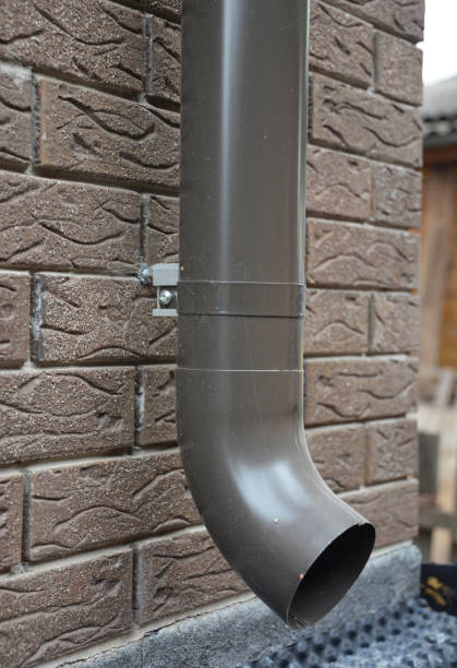istock A close-up on a brown downspout rain gutter pipe attached with a bracket to the foundation of a house. 1295962885