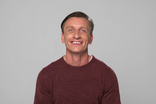 Portrait of smiling mature man standing against grey background.